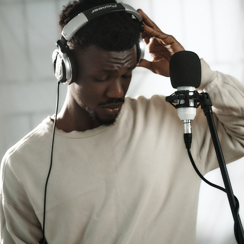 A podcaster in a studio with headphones, standing in front of a microphone.