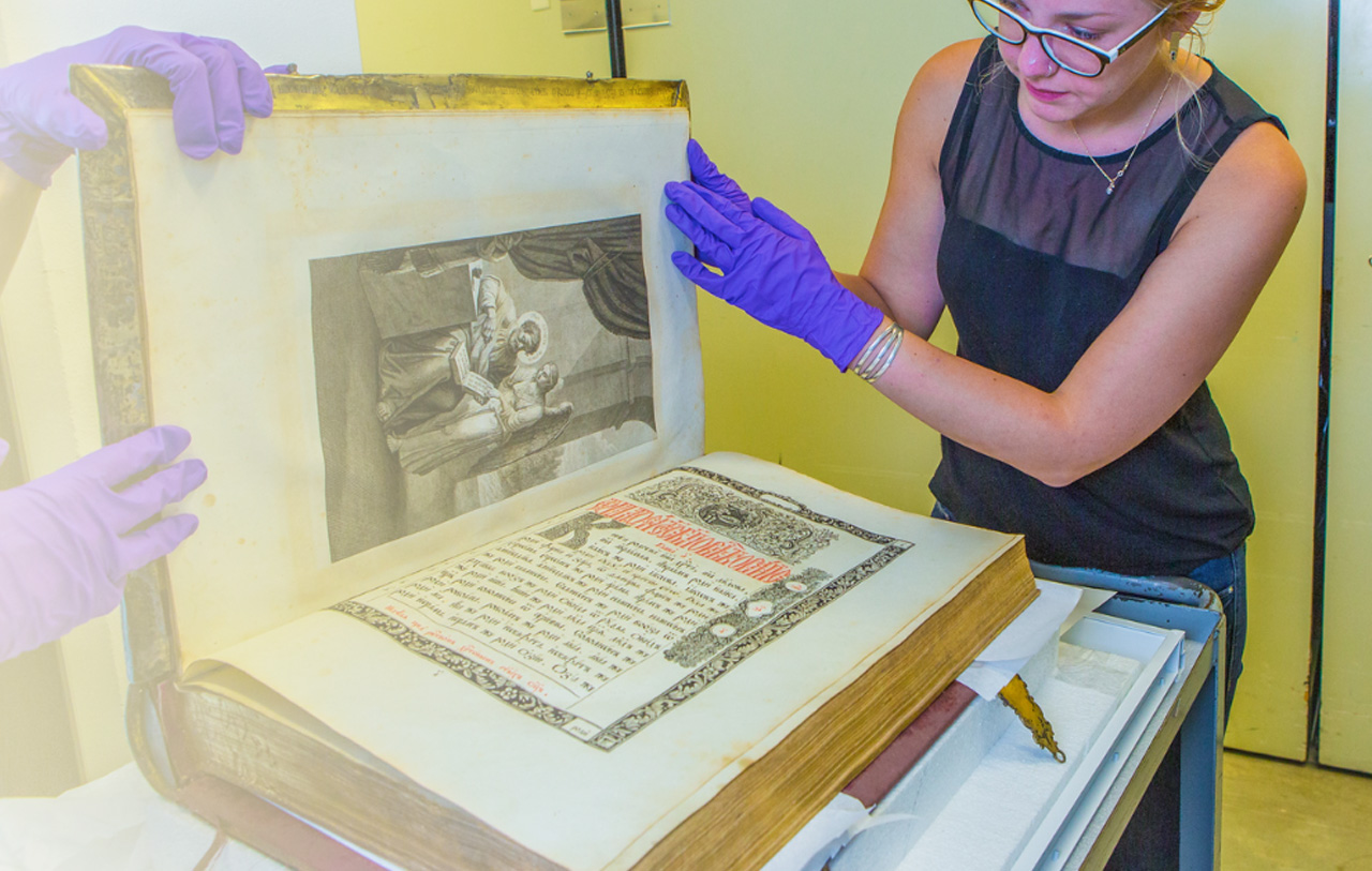 A student assists in handling a book in the collection of the Museum of the North.